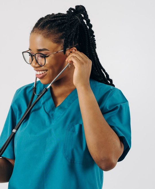 Nurse in teal scrubs smiling, putting on a stethoscope