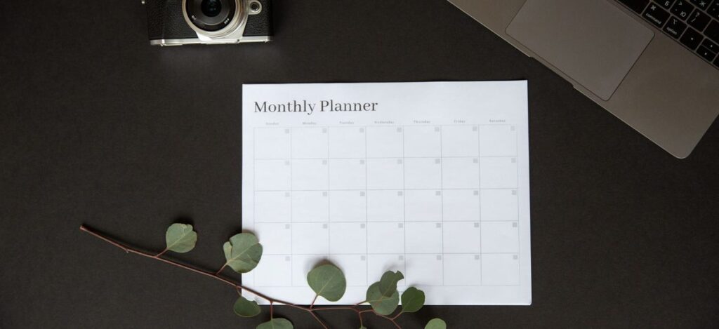 Monthly planner sheet on a desk with a laptop and camera