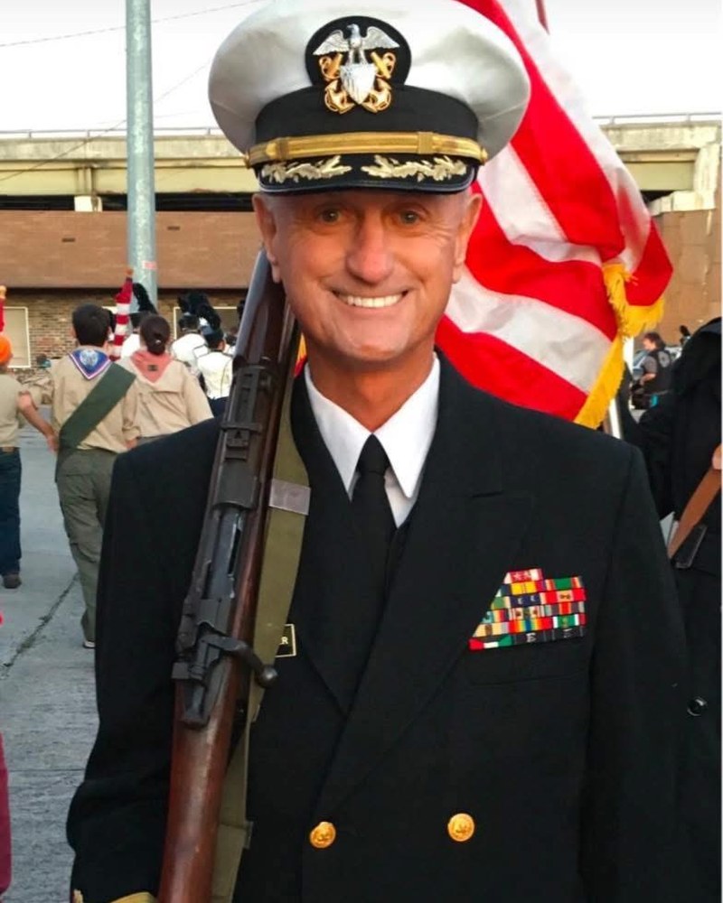 Capt. M. Ron Eslinger, CRNA, smiling in United States Navy dress blues with a flag behind him